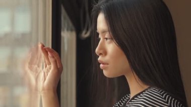 Çekici genç Asyalı bir kadın pencereden dışarı bakıyor. Evde duruyor.