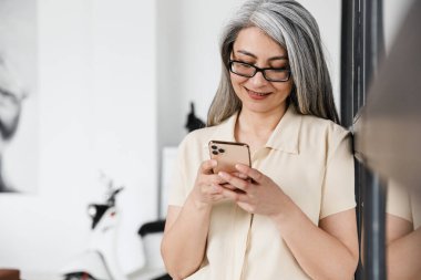 Mutlu, mutlu, olgun bir iş kadınının evde cep telefonu kullanırken görüntüsü.
