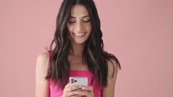 Zadowolona Młoda Kobieta Używa Swojego Smartfona Różowym Tle — Wideo stockowe