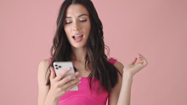 Удивлённая Эмоциональная Молодая Женщина Печатает Своем Смартфоне Изолированный Розовом Фоне — стоковое видео