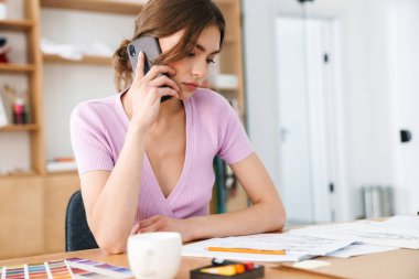 Kapalı alanda cep telefonuyla konuşan ciddi konsantre genç kadın tasarımcının görüntüsü