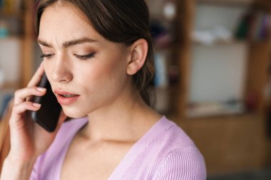 Kapalı alanda cep telefonuyla konuşan ciddi konsantre genç kadın tasarımcının görüntüsü