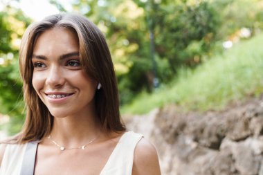 Parkta yürürken diş teli takan, gülümseyen beyaz bir kadın resmi.