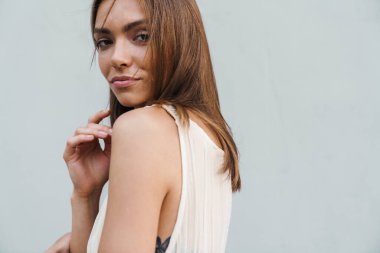 Kameraya bakarken gri duvarın üzerinde poz veren memnun genç kadın görüntüsü.