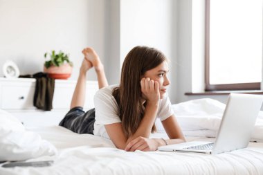 Yatakta dinlenirken dizüstü bilgisayar kullanan çekici genç bir kadın.