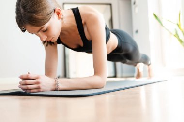 Çekici genç kadın evde çalışıyor, yoga egzersizi yapıyor mavi minder üzerinde, kalas egzersizi yapıyor.