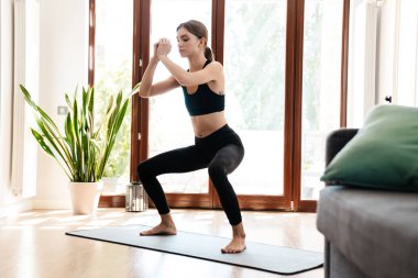 Evde minder üzerinde çalışırken yoga yapan genç bir kadının görüntüsü.