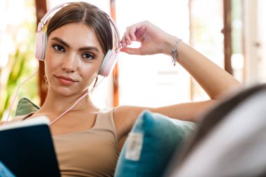 Güzel genç bir kadın kulaklıkla müzik dinliyor, kanepeye bir günlük yazıyor.