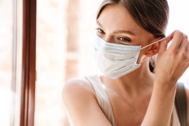 Kapalı alanda tıbbi maske takan genç bir kadına yaklaş.