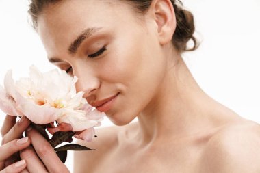 Güzel, gülümseyen, üstsüz bir kadının portresi. Beyaz arka planda izole edilmiş çiçekleri kokluyor.