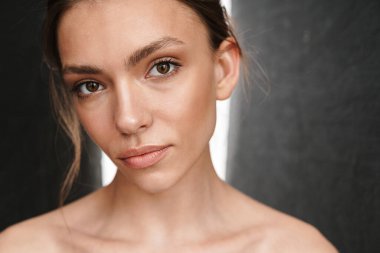 Gri arka planda tek başına duran güzel, beyaz tenli, üstsüz bir kadın resmi.