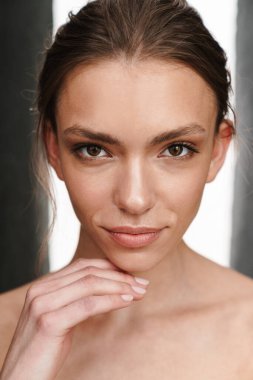 Gri arka planda tek başına duran güzel, beyaz tenli, üstsüz bir kadın resmi.