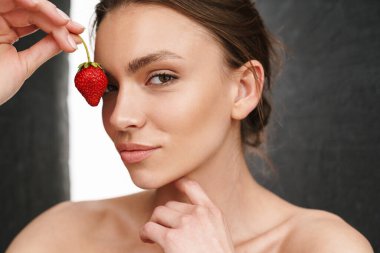 Gri arka planda çilek tutan güzel, beyaz, genç, esmer kadın resmi.