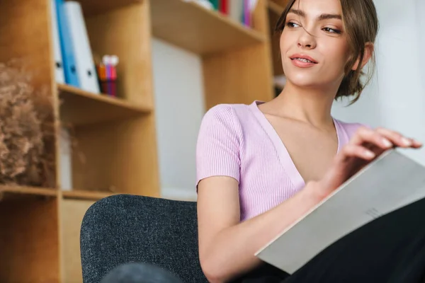 Güzel Bir Kadının Kitap Okurken Parlak Bir Ofiste Koltukta Otururken — Stok fotoğraf