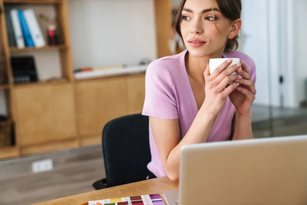 办公室里用手提电脑喝咖啡的漂亮女设计师形象 — 图库照片