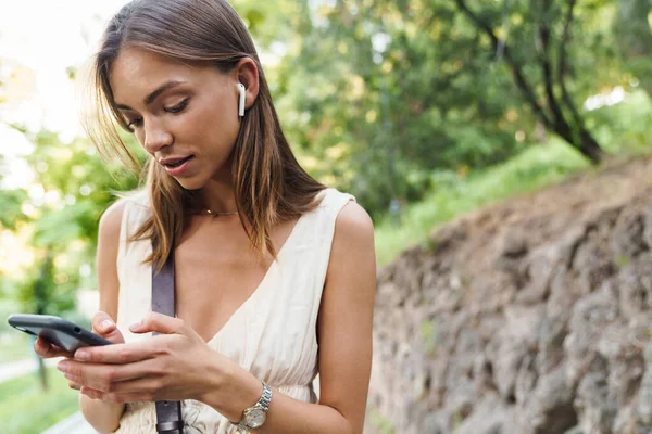 Kép Fiatal Kaukázusi Barna Visel Fülhallgató Gazdaság Mobiltelefon Séta Közben — Stock Fotó