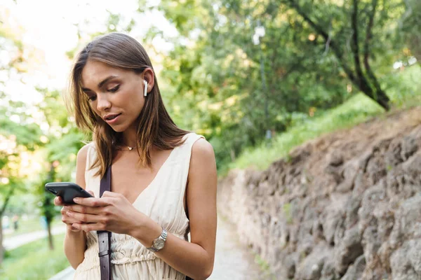 Kép Fiatal Kaukázusi Barna Visel Fülhallgató Gazdaság Mobiltelefon Séta Közben — Stock Fotó