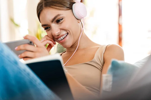 Hermosa Joven Escuchando Música Con Auriculares Escribiendo Diario Sofá Usando — Foto de Stock