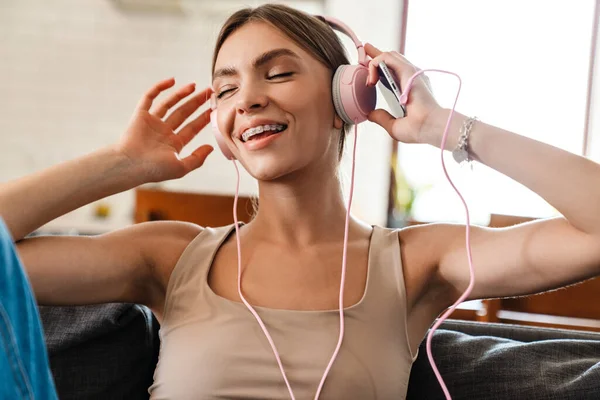 Relaxed woman listening to music with headphones at home, holding mobile phone
