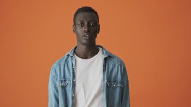 Sakin bir Afrikalı Amerikalı genç adam, turuncu bir arka planda tek başına kameraya bakıyor.