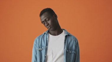 Uyuyan Afrikalı Amerikalı genç bir adam uyanıyor ve turuncu bir arka planda tek başına kameraya bakıyor.
