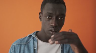 Afro-Amerikan bir gencin yakından çekilmiş görüntüsü turuncu bir arka planda tek başına dikiliyor.