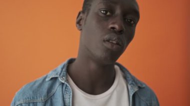 Çekici bir Afrikalı Amerikalı genç adamın, turuncu arka planda tek başına aynaya baktığı yakın plan görüntüsü.