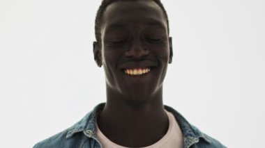 Gülümseyen Afrikalı Amerikalı genç bir adamın yakından görüntüsü mavi arka planda tek başına kameraya doğru başını sallıyor.