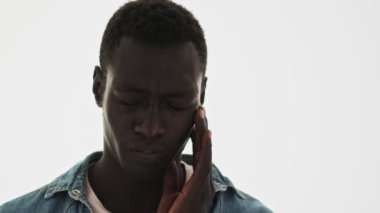 Sıkılmış bir Afrikalı Amerikalı gencin yakın plan görüntüsü mavi arka planda tek başına duran kafasına dokunuyor.