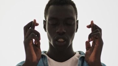 Sakin, Afro-Amerikan bir gencin yakın plan görüntüsü mavi bir arka plan üzerinde izole edilmiş bir dilek diliyor.