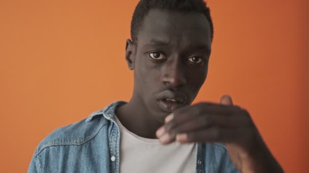 オレンジ色の背景の上に孤立して立っているのを見ているアフリカ系アメリカ人の若者のクローズアップビュー — ストック動画