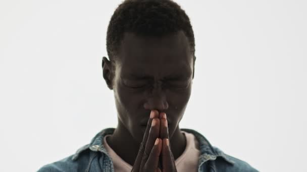 魅力的なアフリカ系アメリカ人の若者が青い背景の上に孤立した何かのために祈っている — ストック動画