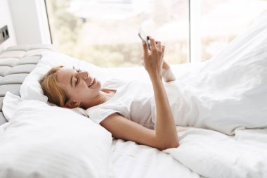 Mutlu genç bir kadının cep telefonu kullanırken ve uyurken gülümserken çekilmiş fotoğrafı.