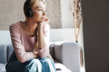 Kafkasyalı bir kadının parlak bir odada koltukta otururken kulaklık taktığı fotoğraf.