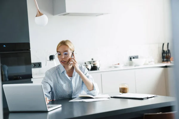 Photo Serious Young Woman Eyeglasses Talking Cellphone While Working Laptop — Stock Photo, Image