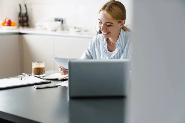 Mutfakta Masada Otururken Bilgisayarla Kağıtlarla Çalışan Mutlu Genç Bir Kadının — Stok fotoğraf