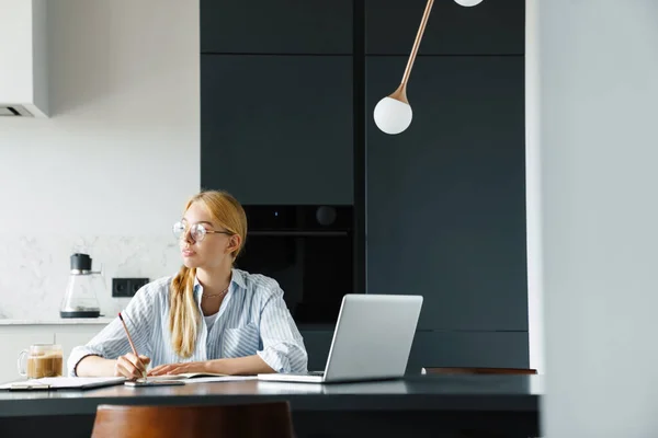 식탁에서 노트북 컴퓨터로 주방에서 일하는 안경을 필기를 여성의 — 스톡 사진