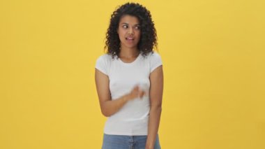 Genç Afrikalı gülümseyen kadın, sarı duvar arkasında izole edilmiş sessizlik jesti gösteriyor.