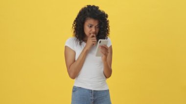 Genç Afrikalı heyecanlı mutlu kadın sarı duvar arkasında izole cep telefonu kullanıyor.