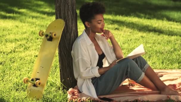 Spokojny Myślący Młody Afrykański Amerykanin Siedzi Trawie Trzymając Książkę Kopiowaniem — Wideo stockowe