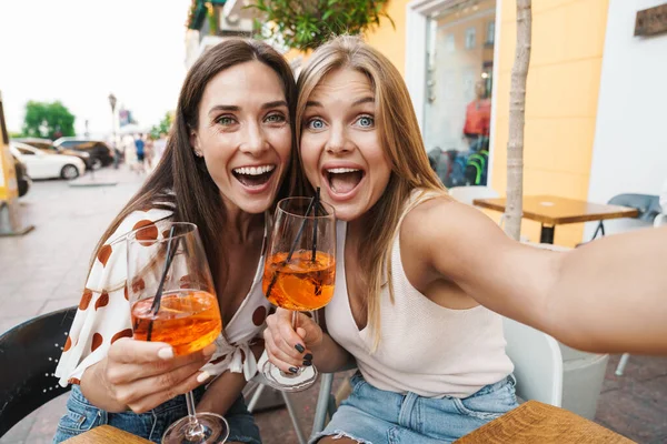 Kafede kokteyl içerken selfie çeken ve sarılan iki kadının görüntüsü.