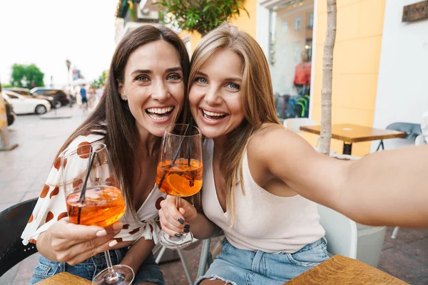 Kafede kokteyl içerken selfie çeken ve gülen iki kadının görüntüsü.