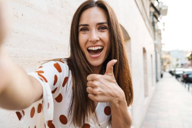 Gülümseyen bir kadının selfie çekerken ve sokaklarda yürürken başparmağını kaldırırken görüntüsü