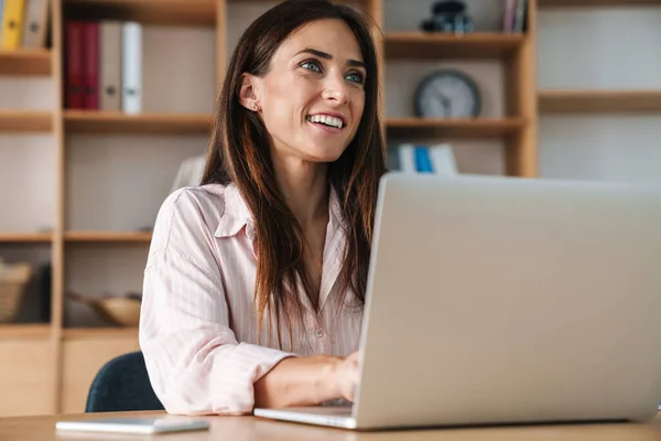 オフィスでノートパソコンと仕事をしながら笑顔で幸せな美しいビジネス女性のイメージ — ストック写真
