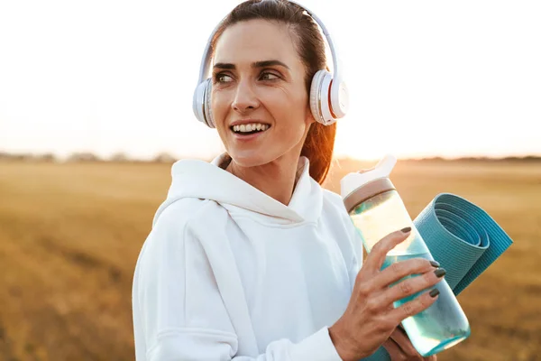 Afbeelding Van Glimlachende Mooie Sportvrouw Hoofdtelefoon Drinkwater Terwijl Het Houden — Stockfoto