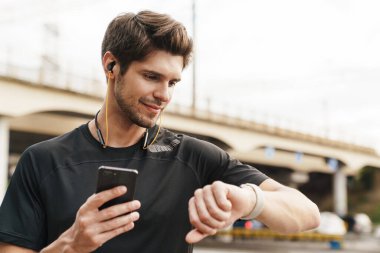 Şehir caddesinde spor yaparken kulaklıkla cep telefonu ve akıllı gözlük kullanan memnun bir sporcu görüntüsü