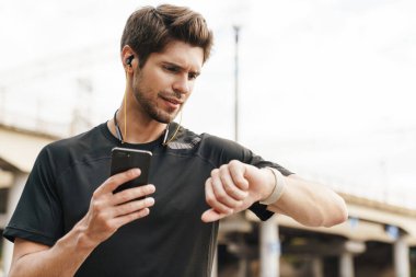 Kulaklıklı kafası karışmış bir sporcunun şehir sokaklarında çalışırken cep telefonu ve akıllı kaset kullanması