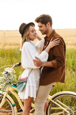 Kırsalda bisiklet sürerken gülümseyen ve kucaklaşan beyaz bir çift.