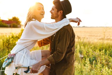 Kırsalda bisiklet sürerken gülümseyen ve kucaklaşan beyaz bir çift.