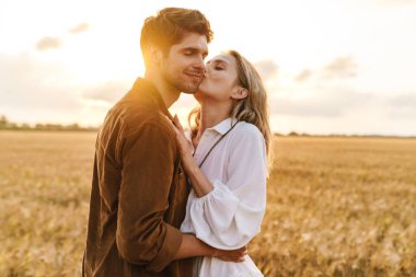 Kırsalda altın tarlada öpüşen ve kucaklaşan beyaz güzel bir çiftin görüntüsü.